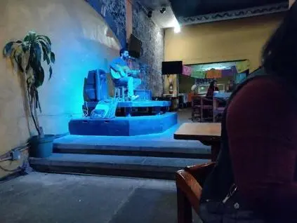 Un músico con guitarra en el escenario de Café Lindo, iluminado de azul